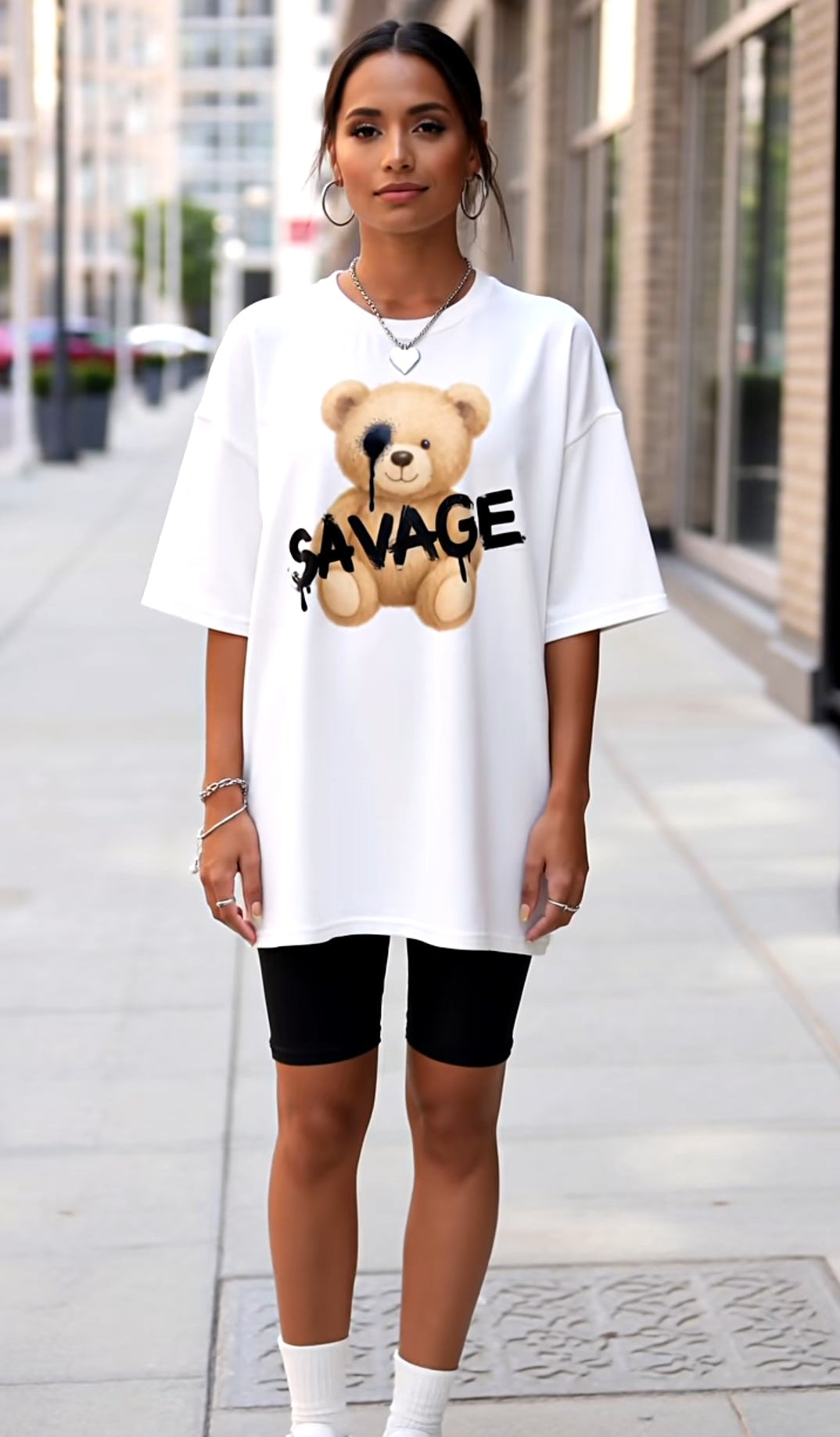 Person wearing a white oversized t-shirt with a bear graphic and 'SAVAGE' text on a city street.