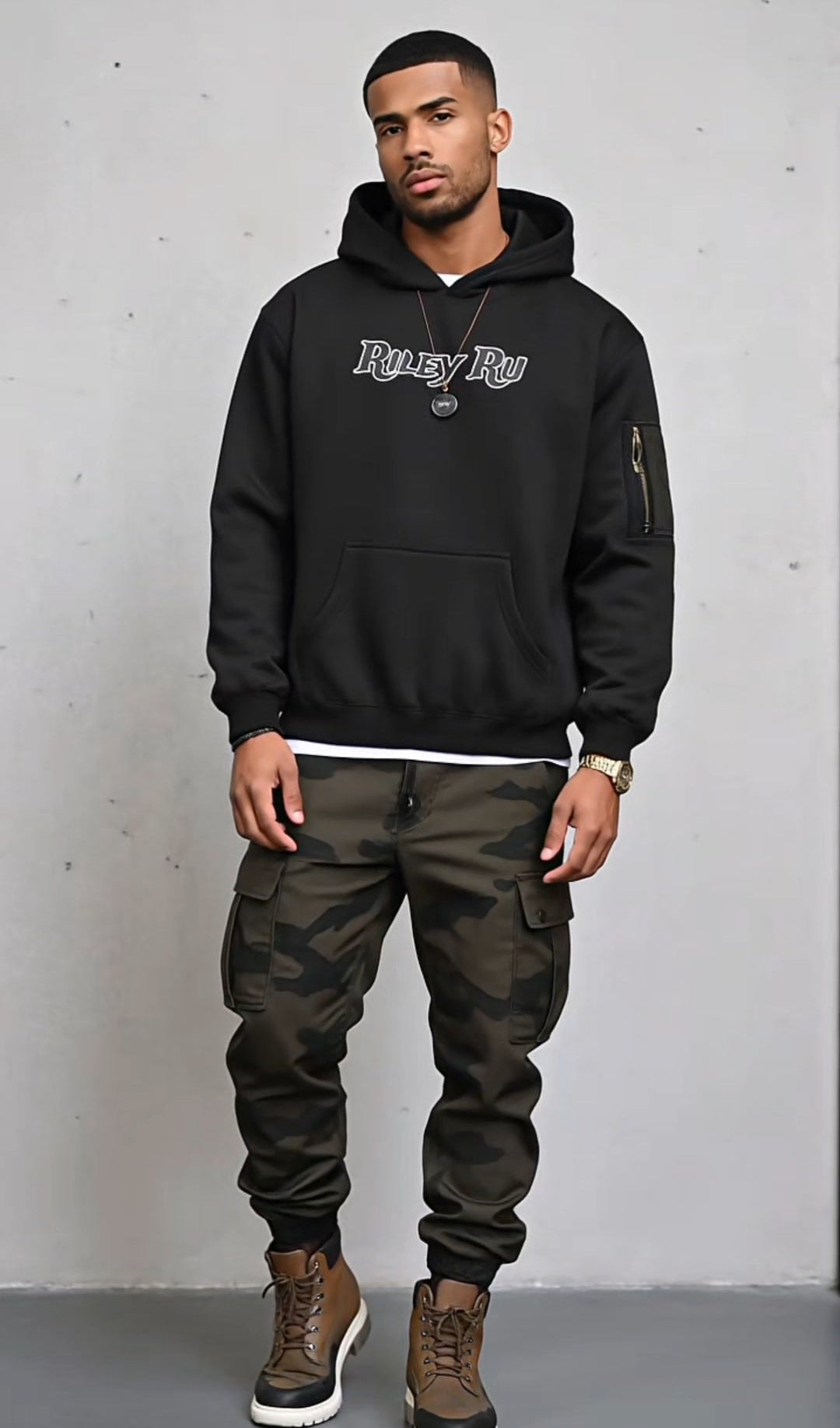Man wearing a black hoodie with text and camouflage pants against a gray background