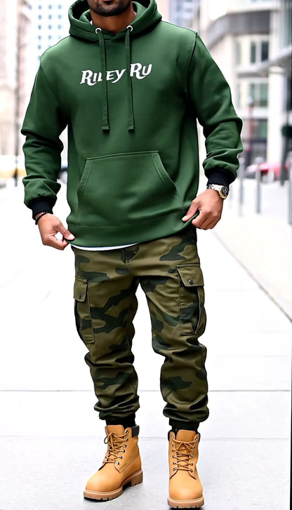 Person wearing a green hoodie and camouflage pants with tan boots on a city street.