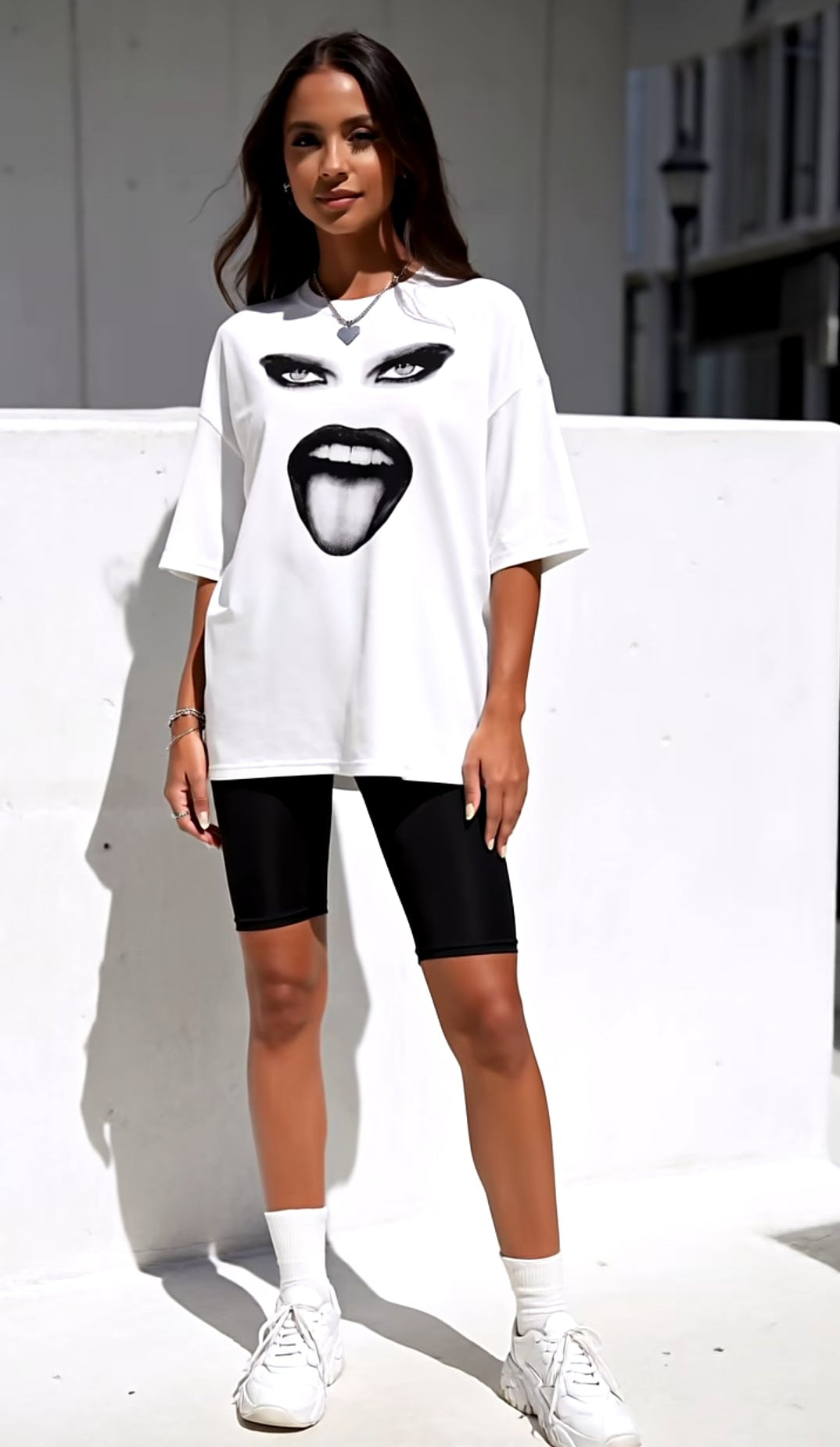 Person wearing a white oversized t-shirt with a graphic design, black shorts, and white sneakers on a plain background.