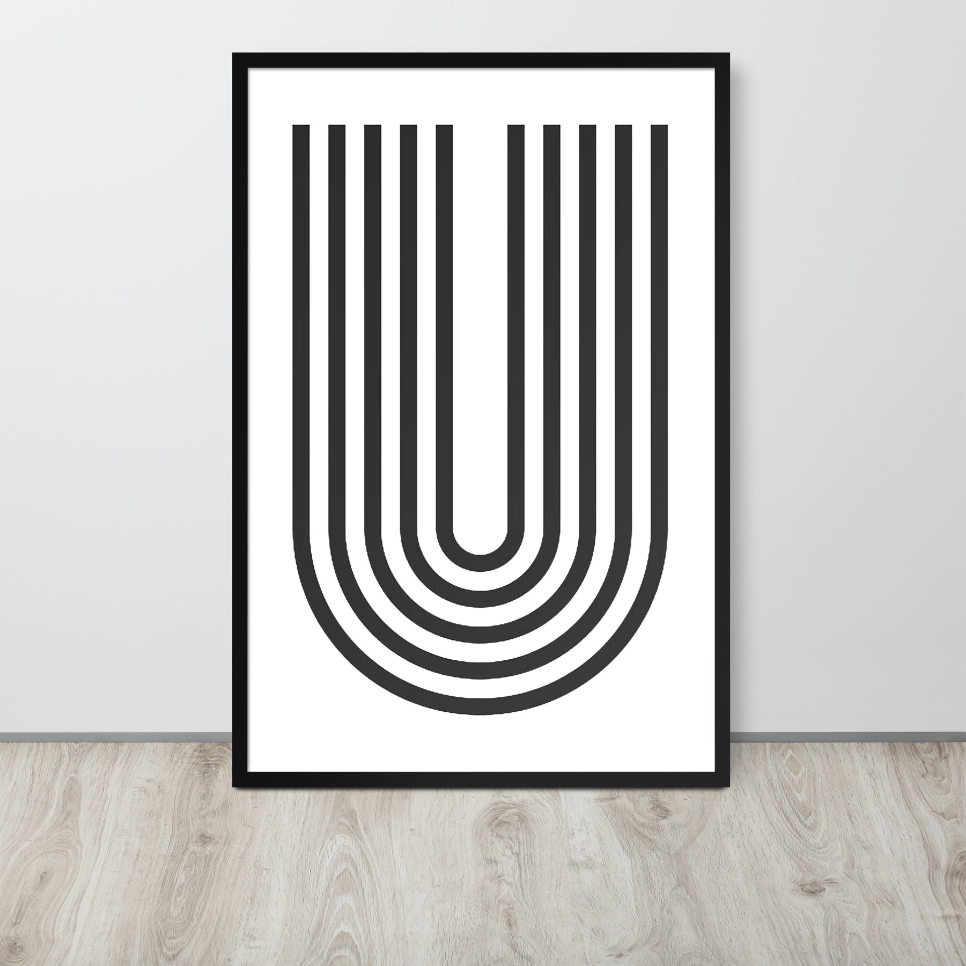 Framed abstract art print with black U-shaped lines on a white background, placed on a wooden floor.