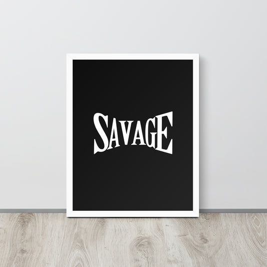 Framed poster with the word 'SAVAGE' on a black background, placed on a wooden surface with a light gray wall in the background.