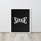 Framed poster with the word 'SAVAGE' on a black background, placed on a wooden surface with a light gray wall in the background.