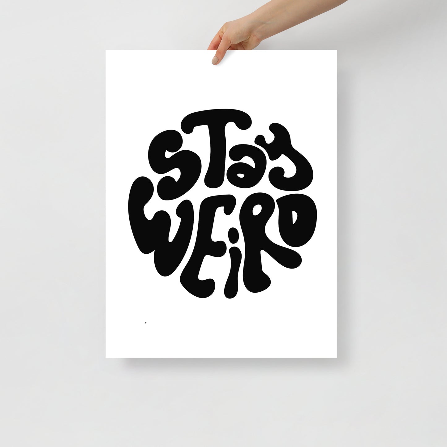 Poster with 'Stay Weird' text held by a hand on a light gray background