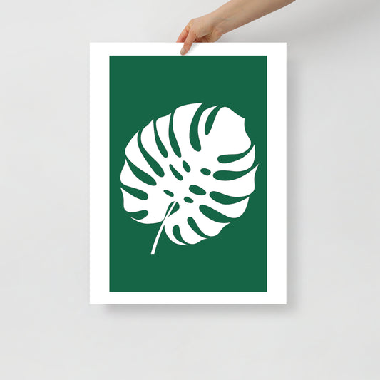Framed poster with a white leaf design on a green background, held by a hand against a light gray background.