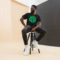 Man sitting on a stool wearing a black t-shirt with green text, black pants, and white sneakers.