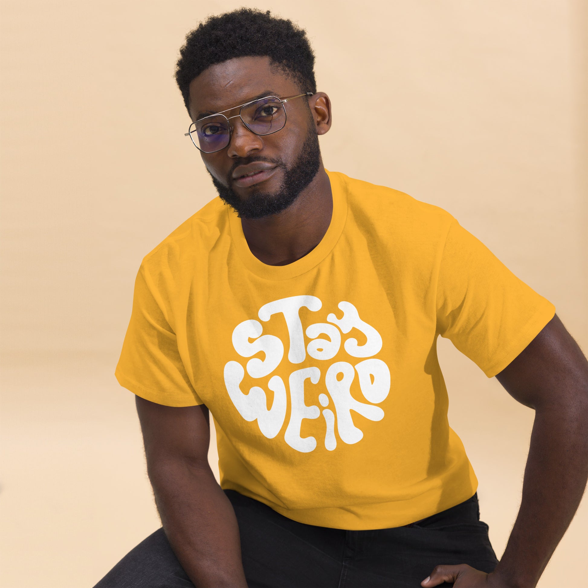 Man wearing a yellow t-shirt with 'Stay Weird' text on a beige background