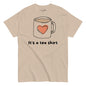 Beige t-shirt with a graphic of a coffee mug with a heart and text 'It's a tea shirt' on a white background