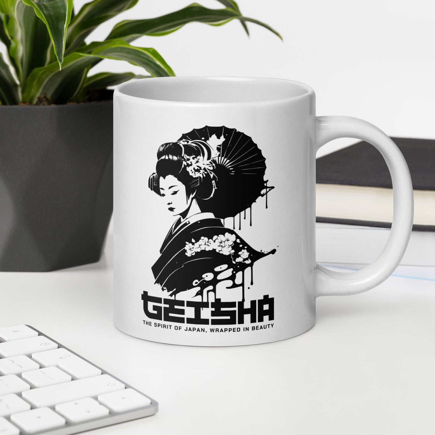 White mug with a black and white design of a geisha and text on a desk with a plant and books in the background.