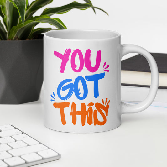 White mug with colorful text 'YOU GOT THIS' on a desk with a plant and books in the background